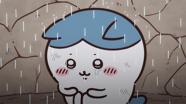 ひび割れた土の壁の前で、雨に打たれながらあごの下で両手をそろえ、目に涙をためているハチワレ。アニメ「ちいかわ」第31話「穴に落ちた①」の場面