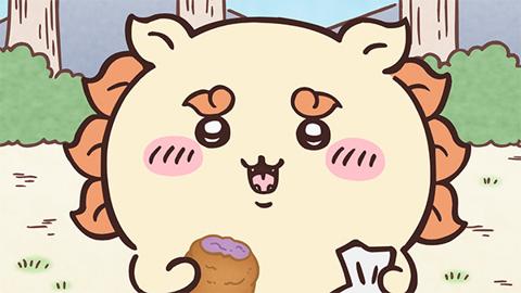 木と草むらのある野原で、シーサーが口を開けてにっこり笑い、片手に紫色のものがのった茶色い揚げ菓子を持っている、アニメ「ちいかわ」第165話「さたぱんびん/さんぴん茶」の場面